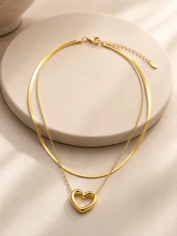 Full view of Amora Duo double-layer gold-tone heart pendant necklace arranged on an ivory jewellery stand
