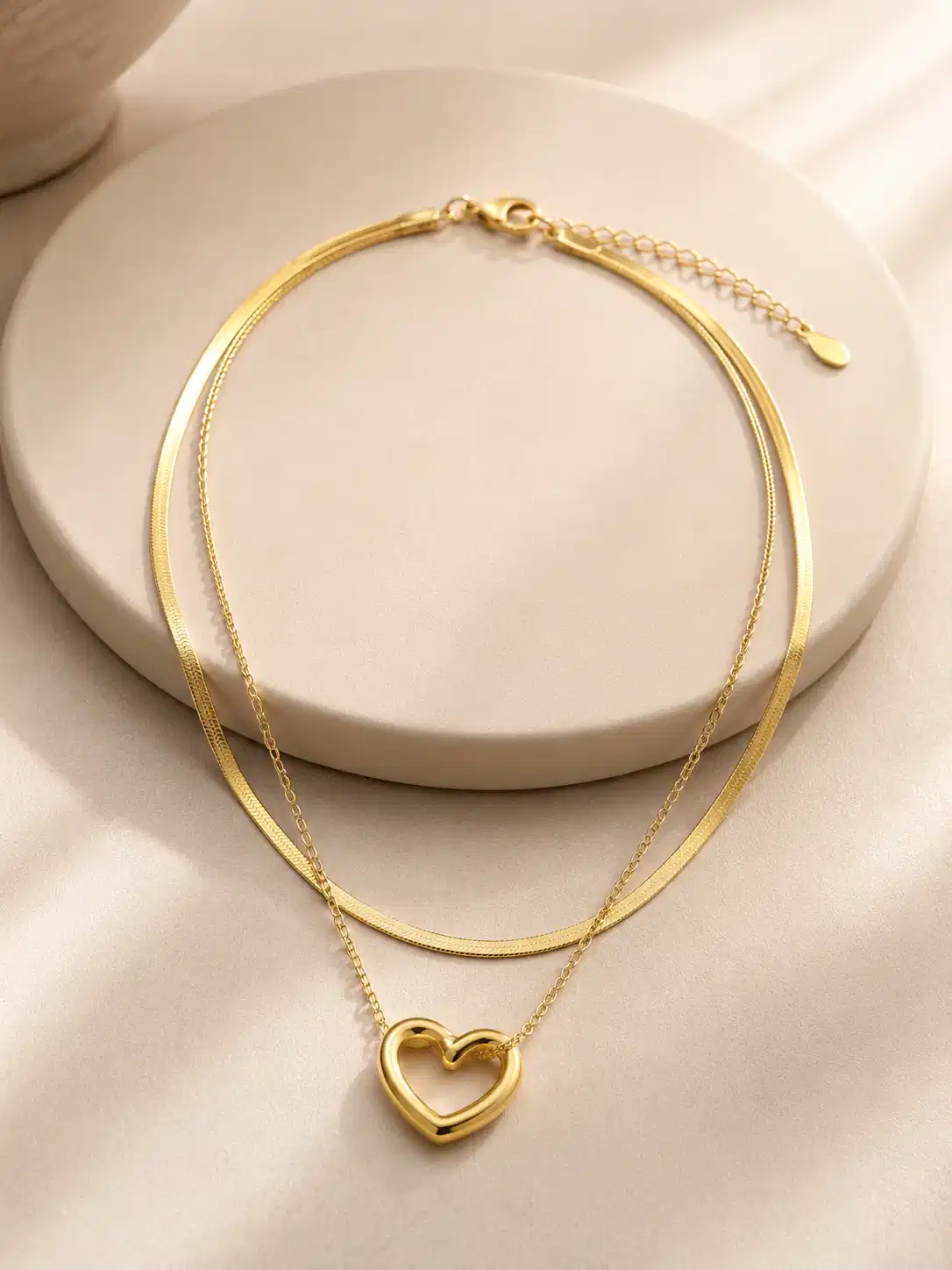 Full view of Amora Duo double-layer gold-tone heart pendant necklace arranged on an ivory jewellery stand