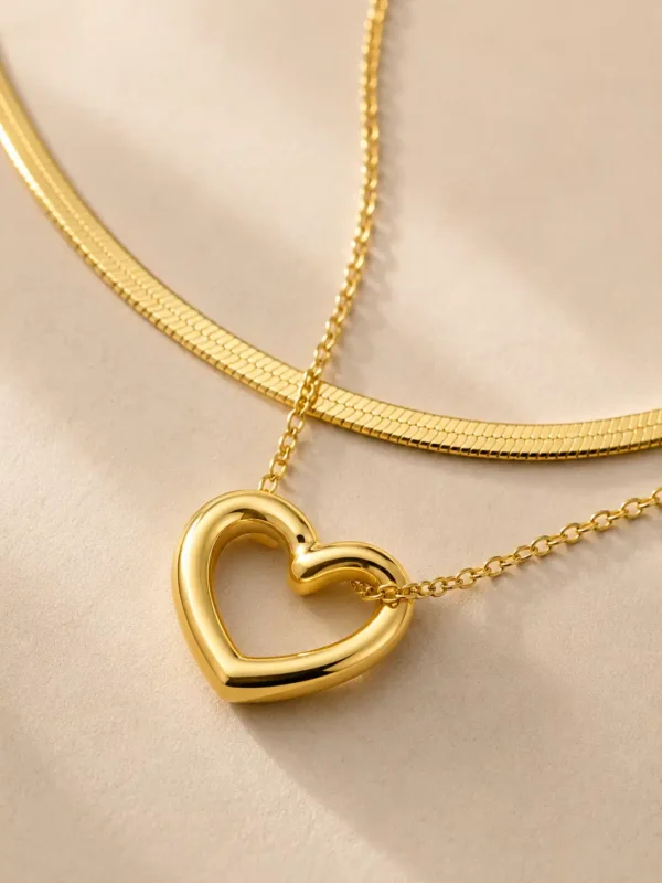 Close-up of the polished open-heart pendant and flat snake chain on the Amora Duo layered necklace