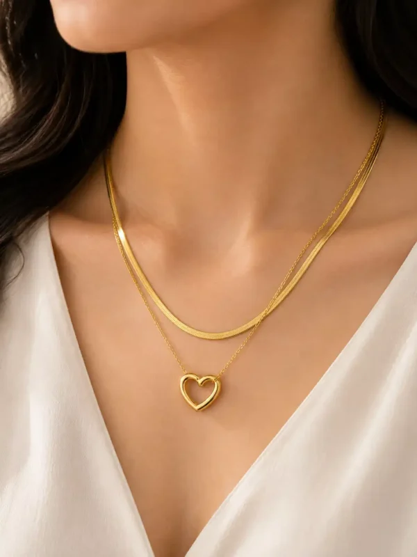 Woman wearing the Amora Duo gold-tone heart layered necklace with a white V-neck blouse