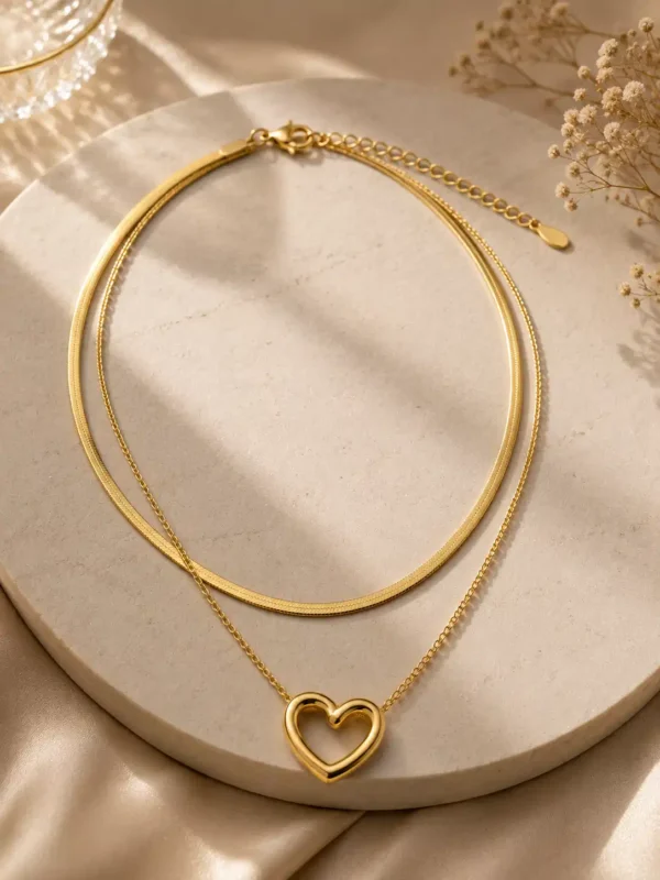 Amora Duo gold-tone double-layer heart necklace displayed on an ivory stone tray in warm sunlight