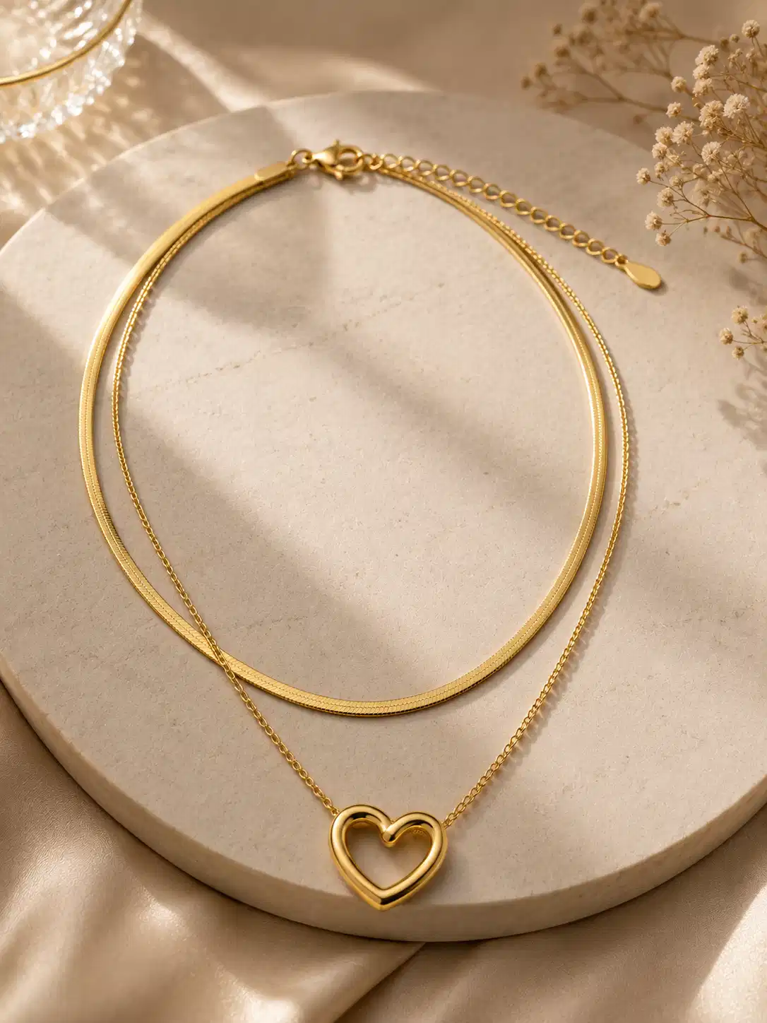 Amora Duo gold-tone double-layer heart necklace displayed on an ivory stone tray in warm sunlight