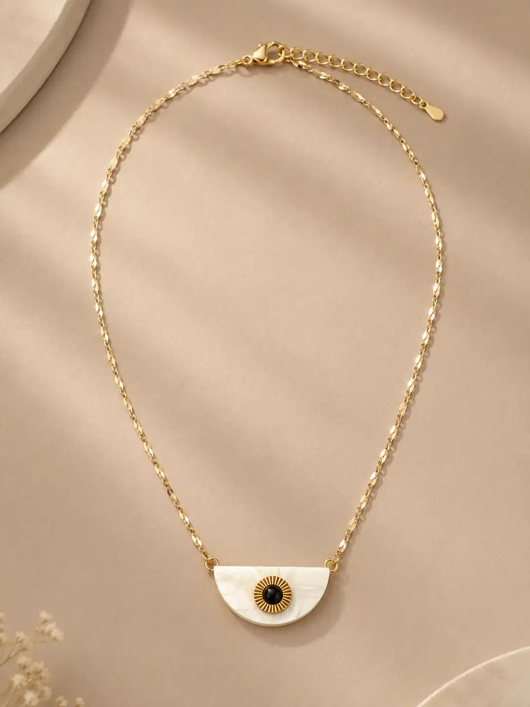 Nivara half-moon evil eye pendant necklace with a white, black and gold-tone design on a faceted chain