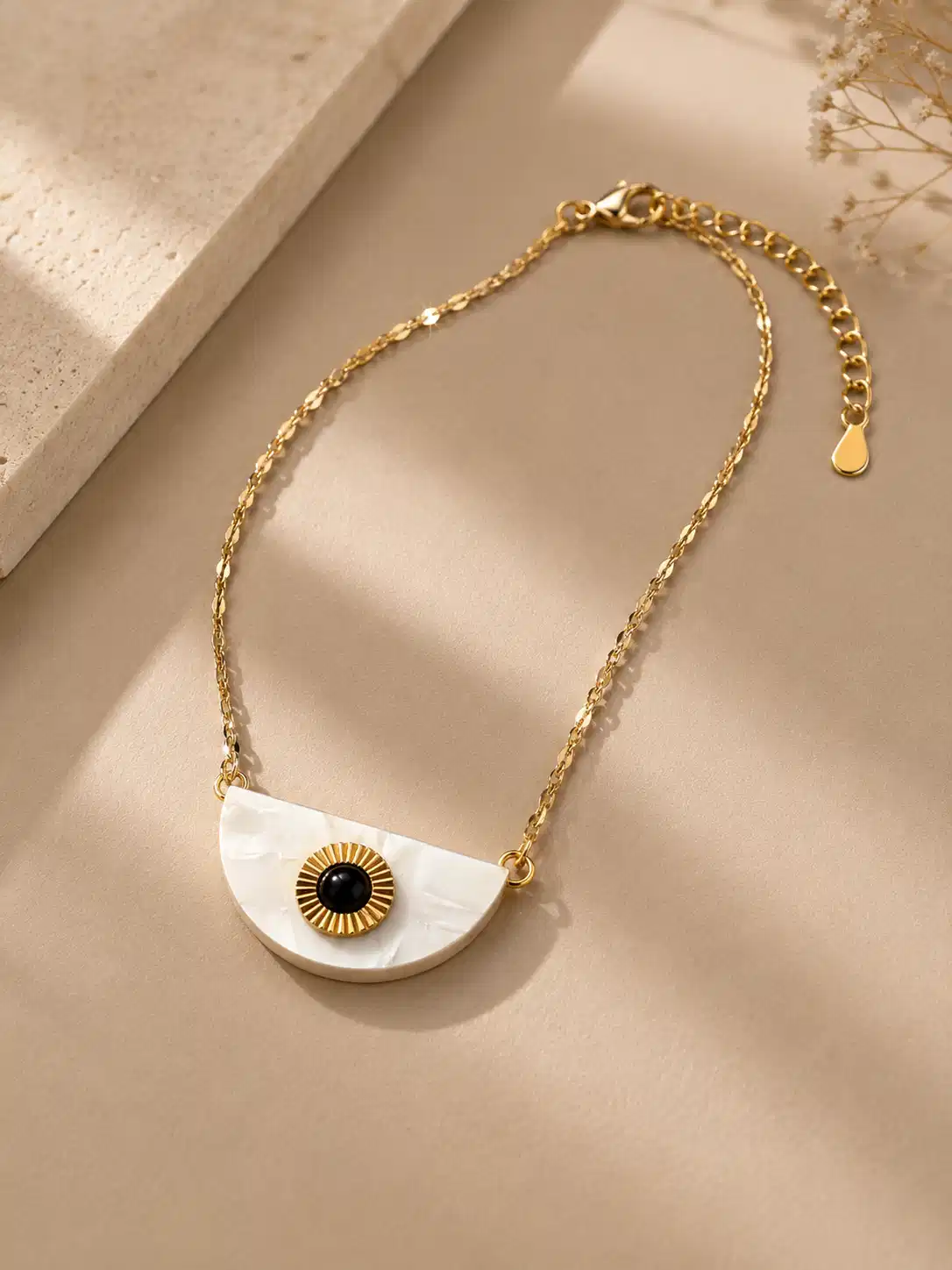Angled view of Nivara gold-tone evil eye necklace showing the half-moon pendant, lobster clasp and extension chain