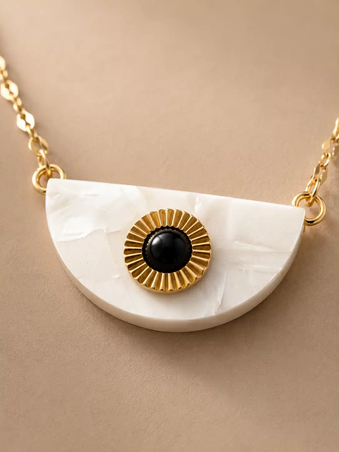 Close-up of Nivara white half-moon pendant with a black circular centre and radiating gold-tone detail