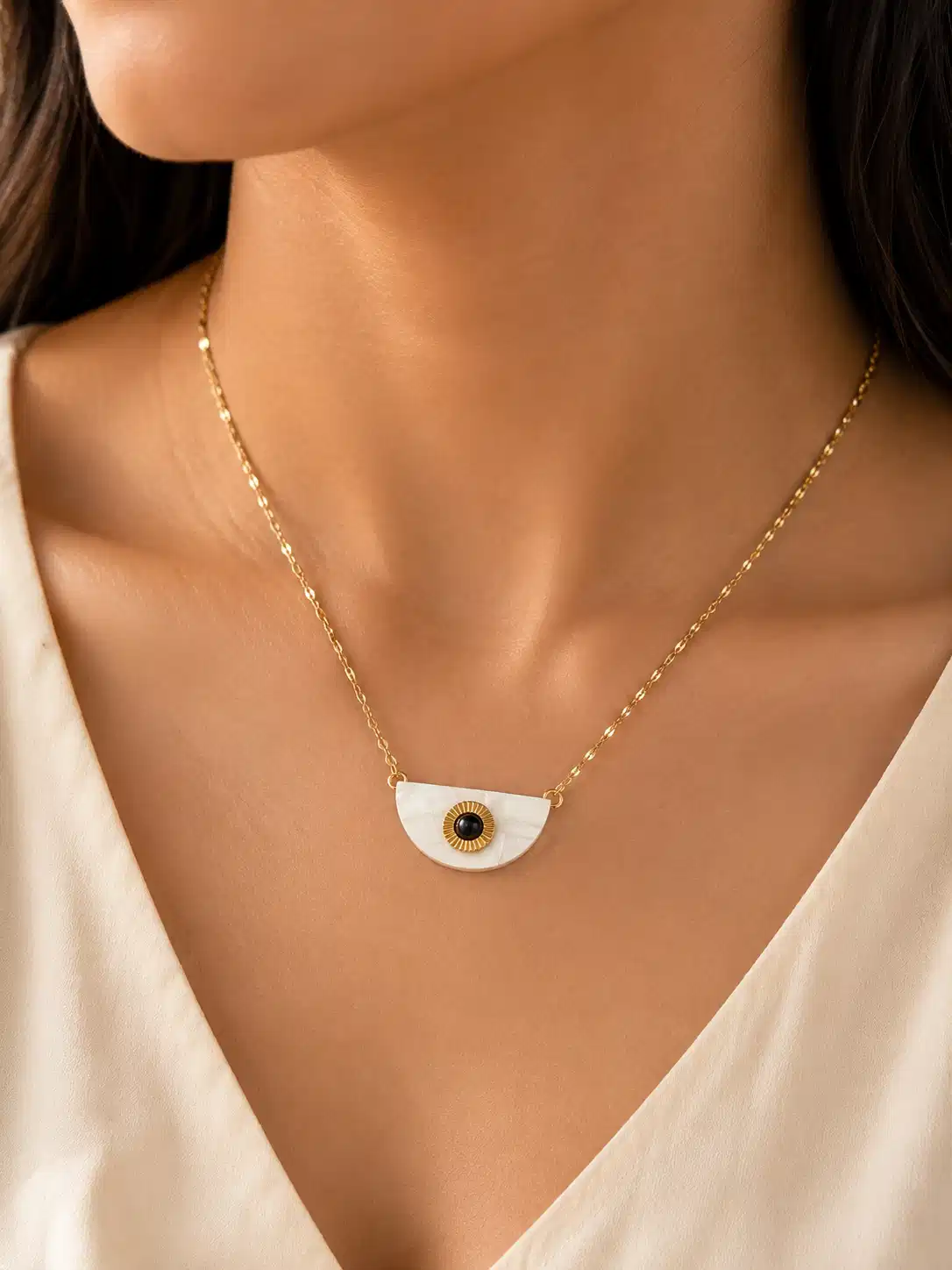 Woman wearing the Nivara half-moon evil eye pendant necklace with a white V-neck blouse