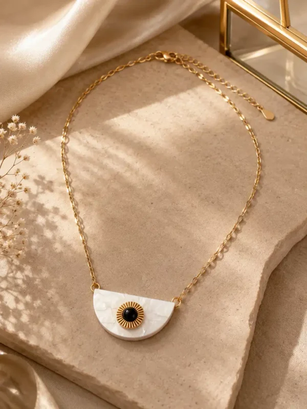 Nivara gold-tone half-moon evil eye necklace arranged on an ivory stone surface in warm sunlight