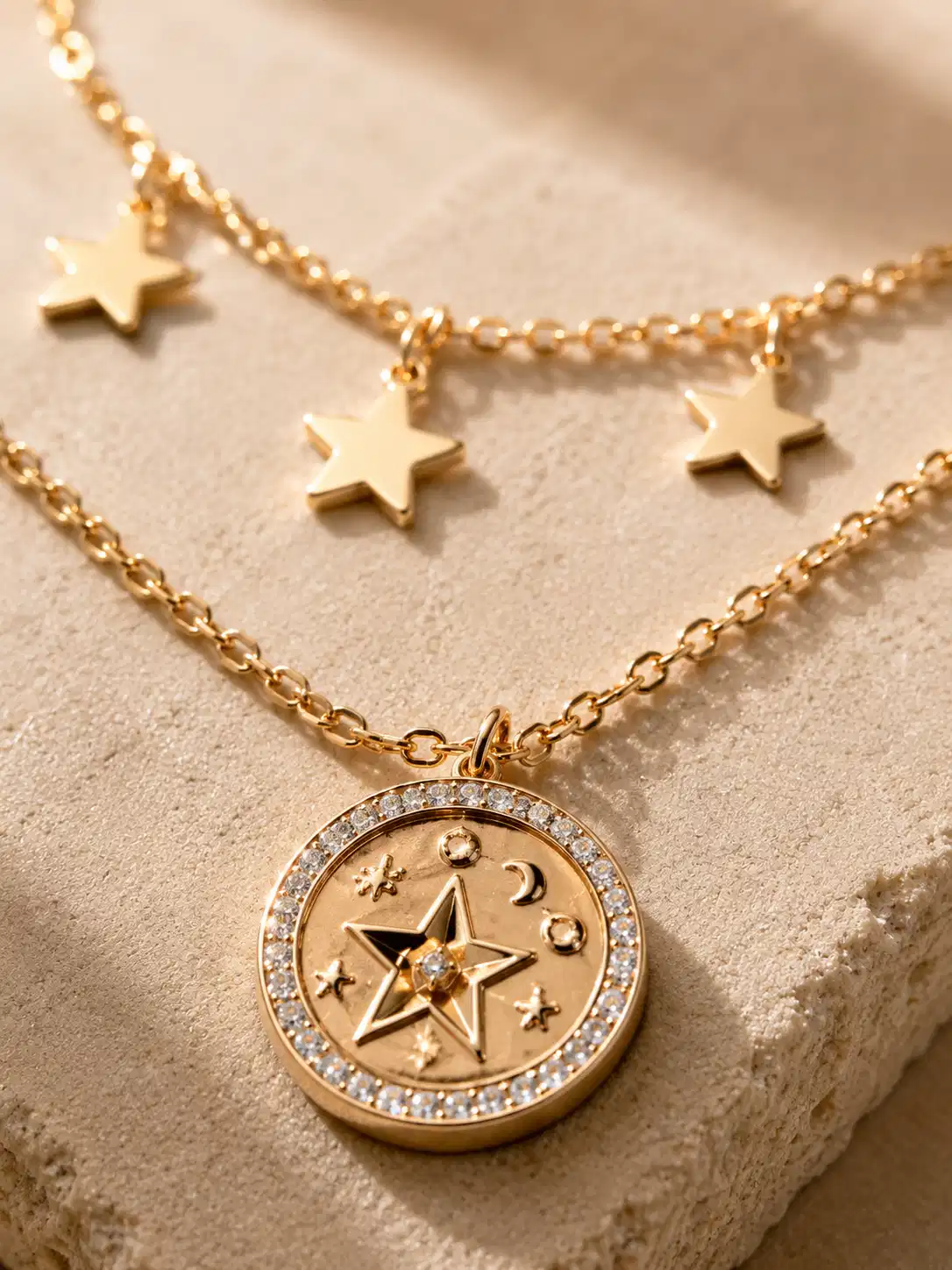 Close-up of five gold-tone star charms and crystal-style celestial medallion on the Lunara layered necklace