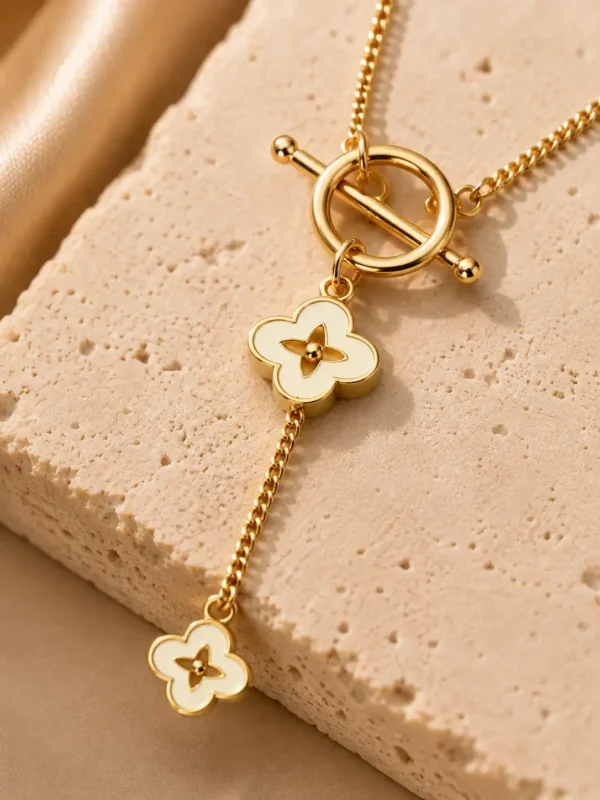 Close-up of the Fiora necklace with a polished gold-tone toggle detail and two ivory four-petal floral charms