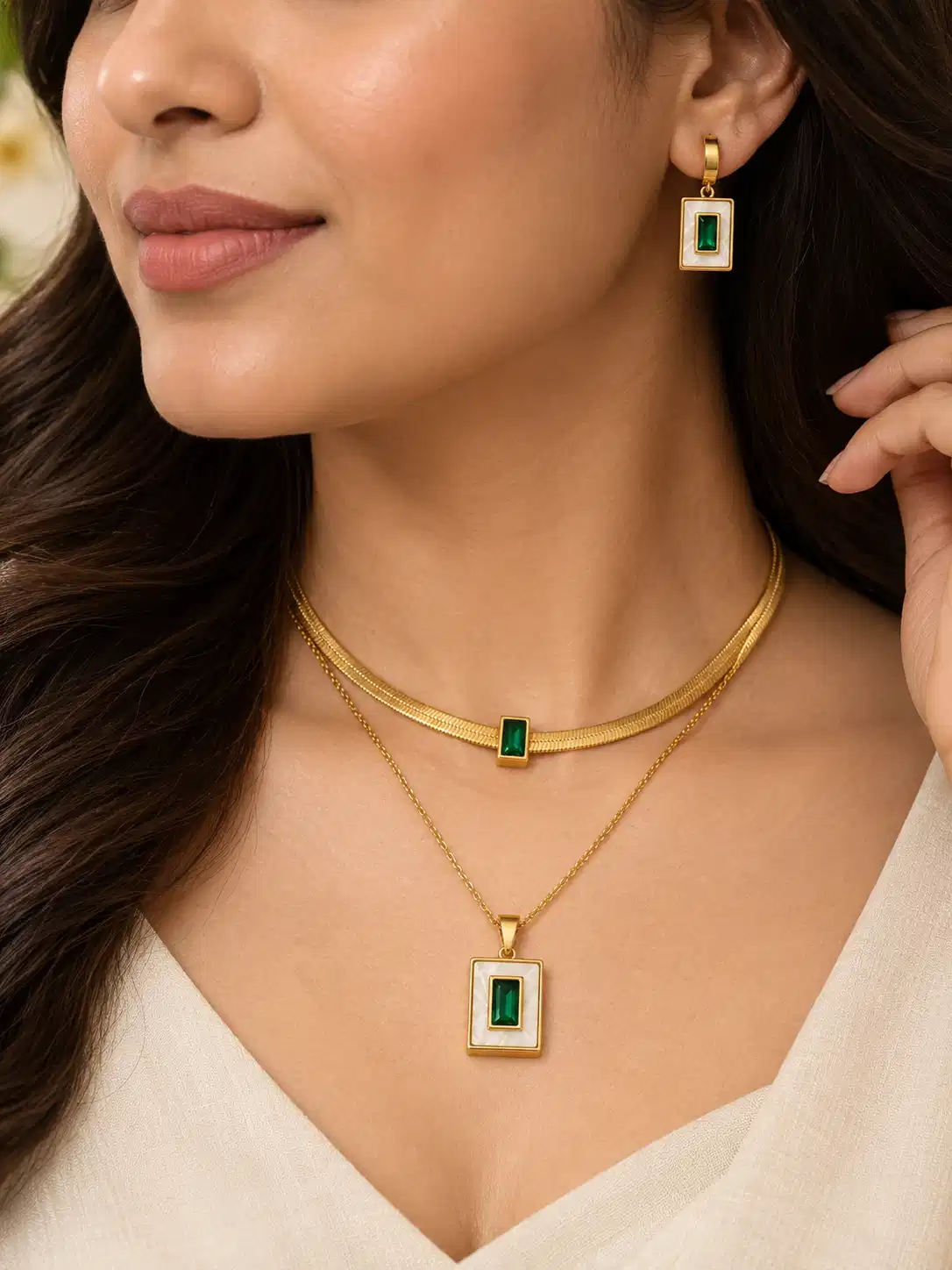 Woman wearing a gold-tone layered necklace and matching earrings with emerald-green rectangular accents