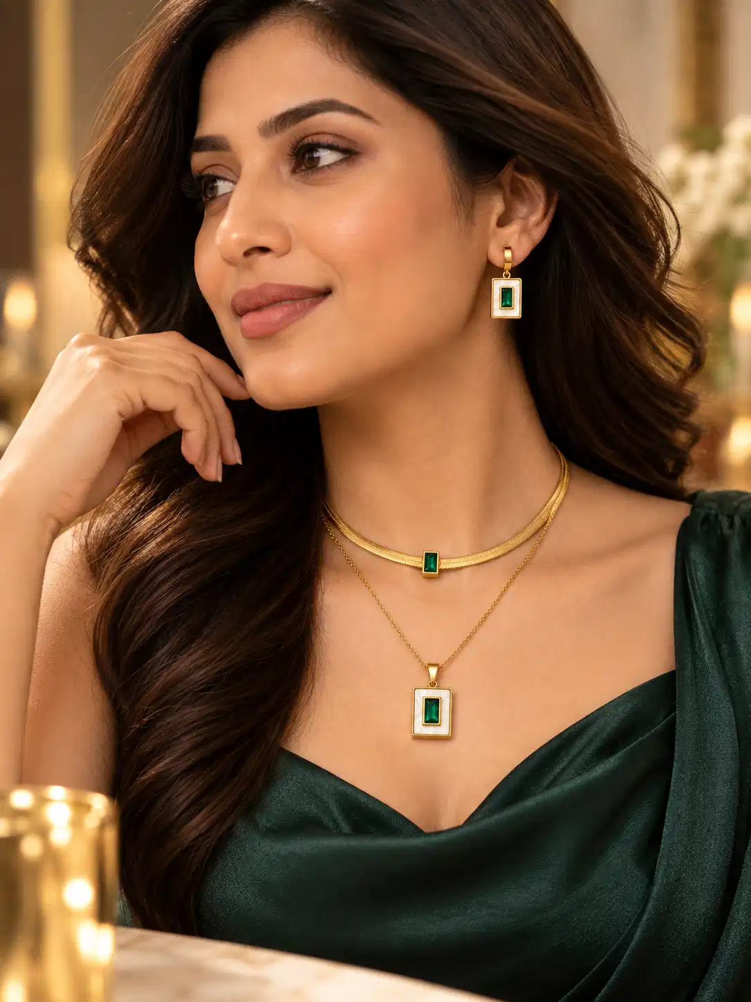 Woman wearing a gold-tone layered necklace and rectangular green earrings with an emerald evening dress