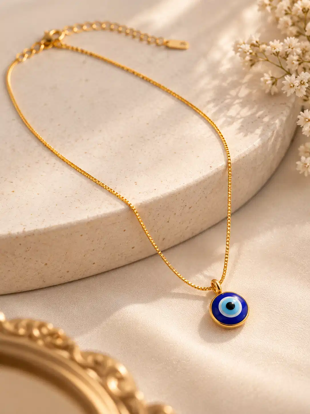 Gold-tone chain with round blue nazar pendant displayed on a neutral stone surface