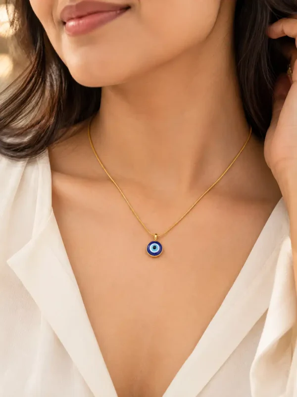 Woman wearing a minimal round blue evil eye necklace with a white V-neck outfit