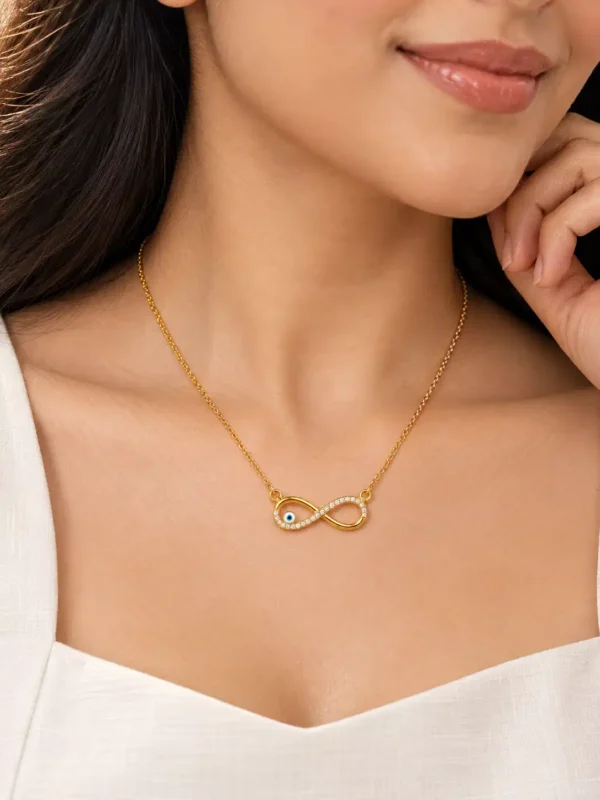 Woman wearing a minimal gold-tone infinity evil-eye necklace with a white outfit