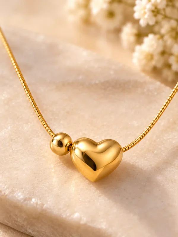 Close-up of smooth mirror-polished 3D heart pendant and round bead on gold-tone necklace