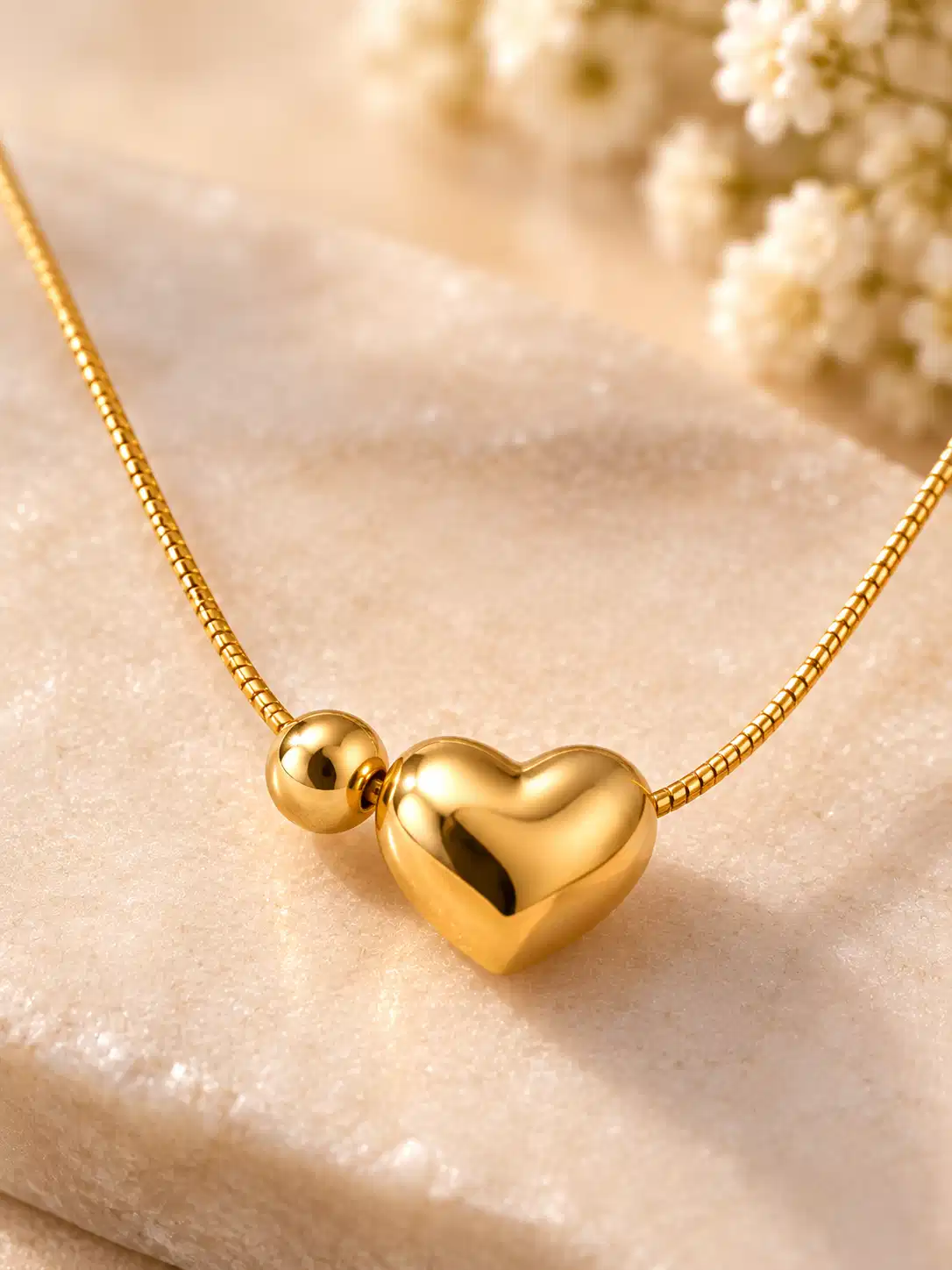 Close-up of smooth mirror-polished 3D heart pendant and round bead on gold-tone necklace