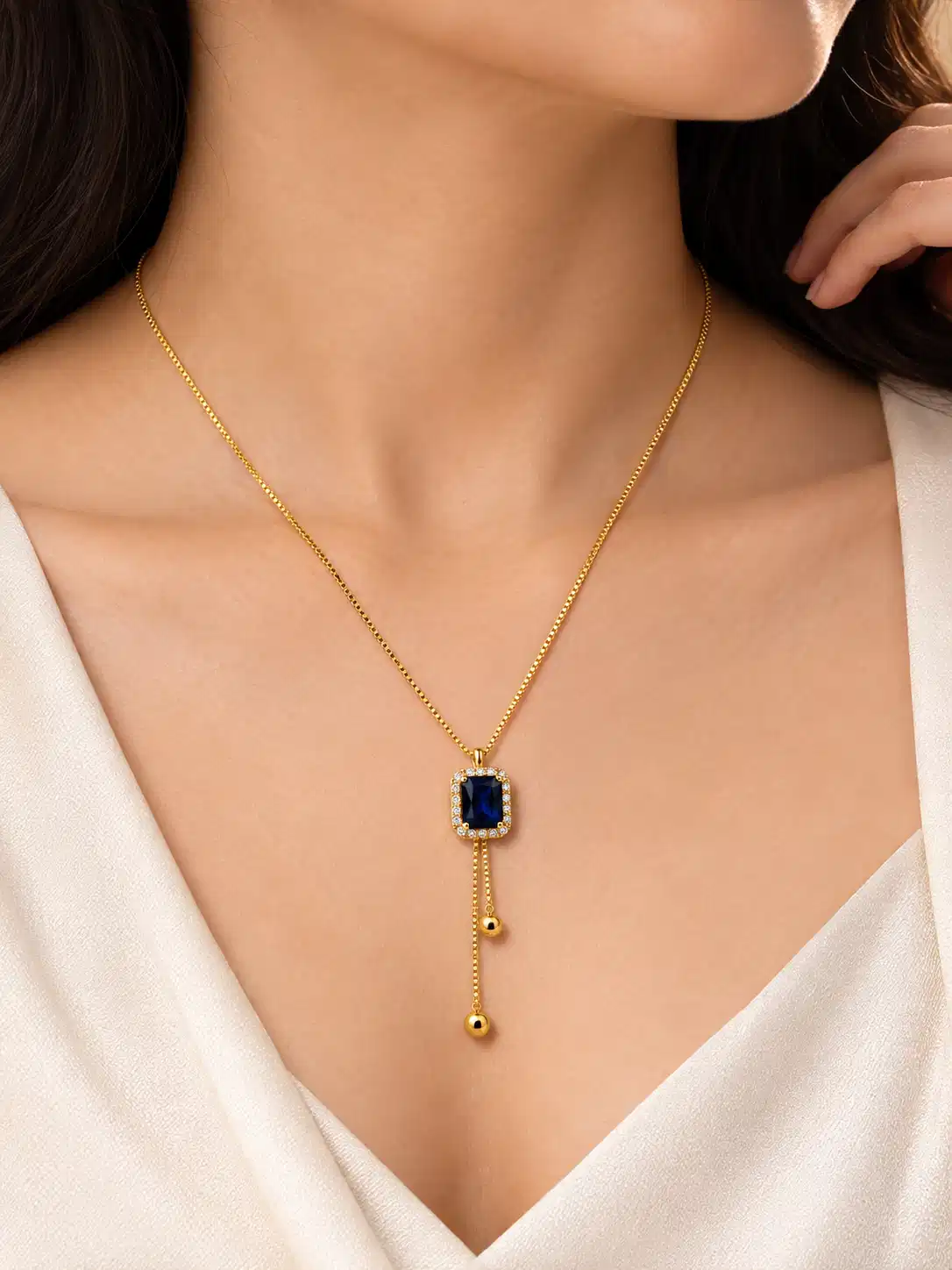 Woman wearing Blue Hour gold-tone Y-drop necklace with deep blue crystal pendant and delicate drops