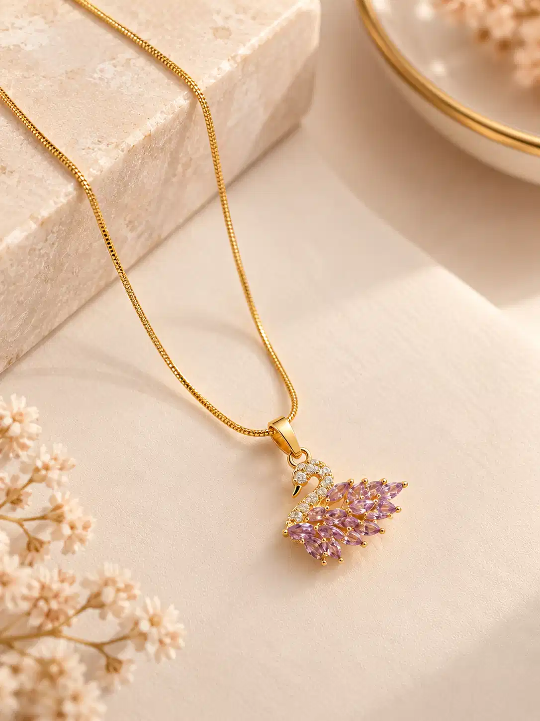 Pink stone swan pendant necklace with gold-tone chain styled on a soft neutral jewellery flat lay
