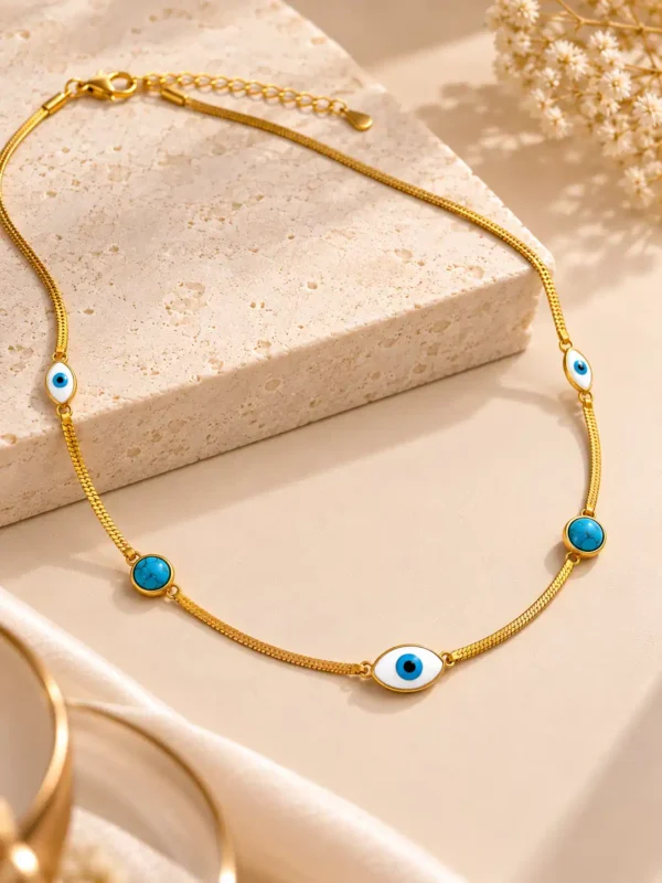 Close-up product photograph highlighting the five decorative elements of the Azure Nazar Grace Necklace: a large central evil eye, two smaller side eye motifs and two round turquoise-look accents with natural-style veining. The balanced gold, white, blue and black palette creates a distinctive yet minimal everyday jewellery look.