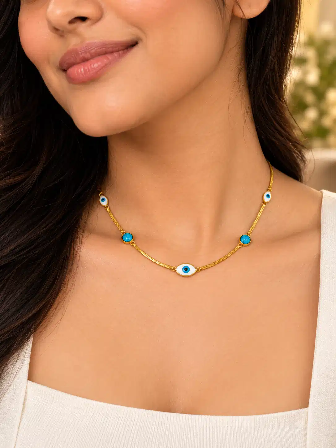 Woman wearing a gold-tone evil eye necklace with turquoise blue accents and a white top