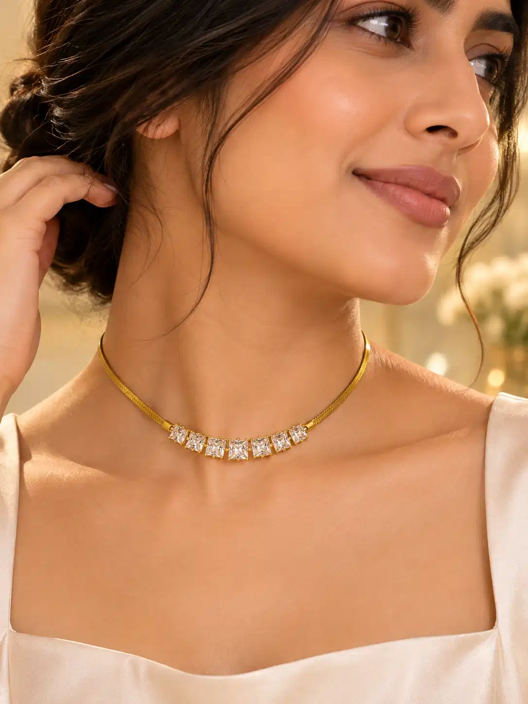 Woman wearing a gold-tone necklace with seven square clear stones styled with an elegant white outfit
