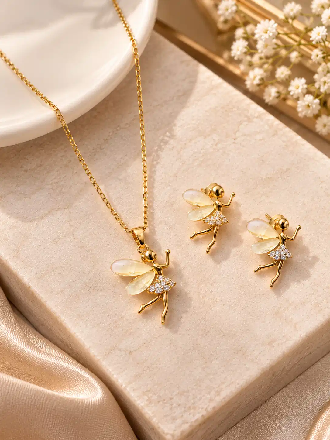 Gold tone fairy necklace and matching earrings with ivory translucent wings displayed on a neutral jewellery surface