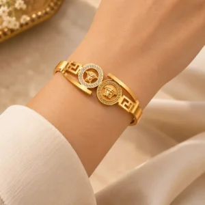 Gold-tone twin medallion statement bangle with crystal halo and Greek-key detailing worn on a woman’s wrist
