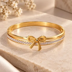 Elara gold-tone crystal bow bangle for women with sculpted ribbon motif and clear crystal row