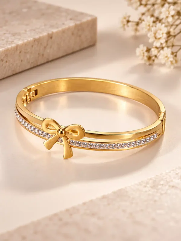Angled view of gold bow bracelet for women with polished rigid band and clear crystal detailing