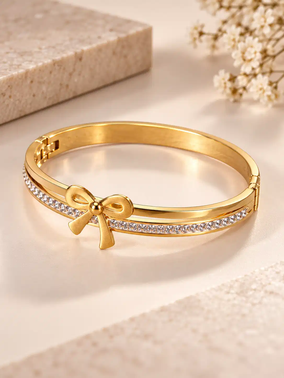 Angled view of gold bow bracelet for women with polished rigid band and clear crystal detailing
