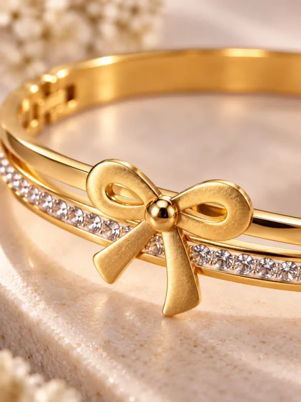 Close-up of sculpted gold ribbon bow and clear crystal row on Elara women's bangle