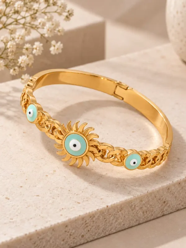 Angled view of a gold evil eye bracelet with turquoise nazar motifs, sunburst centre design and structured hinged bangle.
