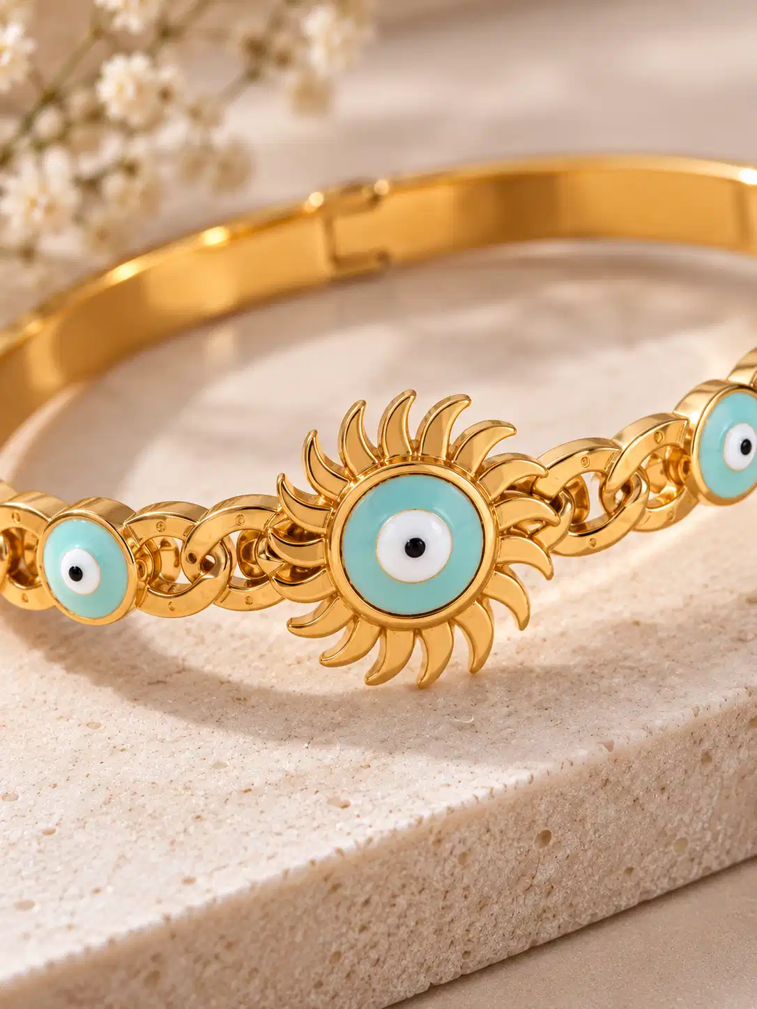 Close-up of turquoise evil eye sunburst motif with white centre, black pupil and sculpted gold detailing on a statement bangle.
