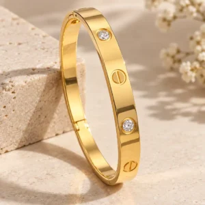 Aurelia gold bangle for women with clear crystal accents and engraved screw-style motifs in a polished structured design.