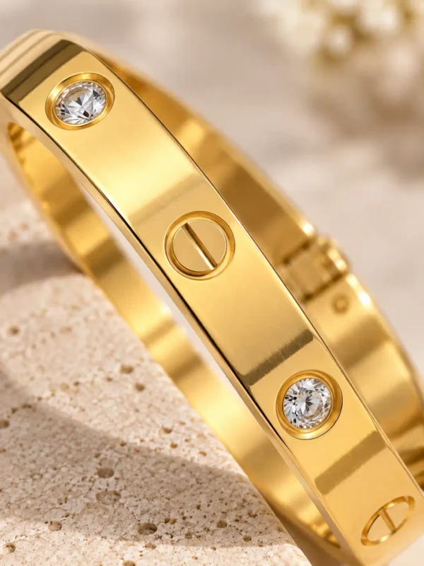 Close-up of Aurelia gold bangle showing round clear crystal settings and polished engraved screw-style details.