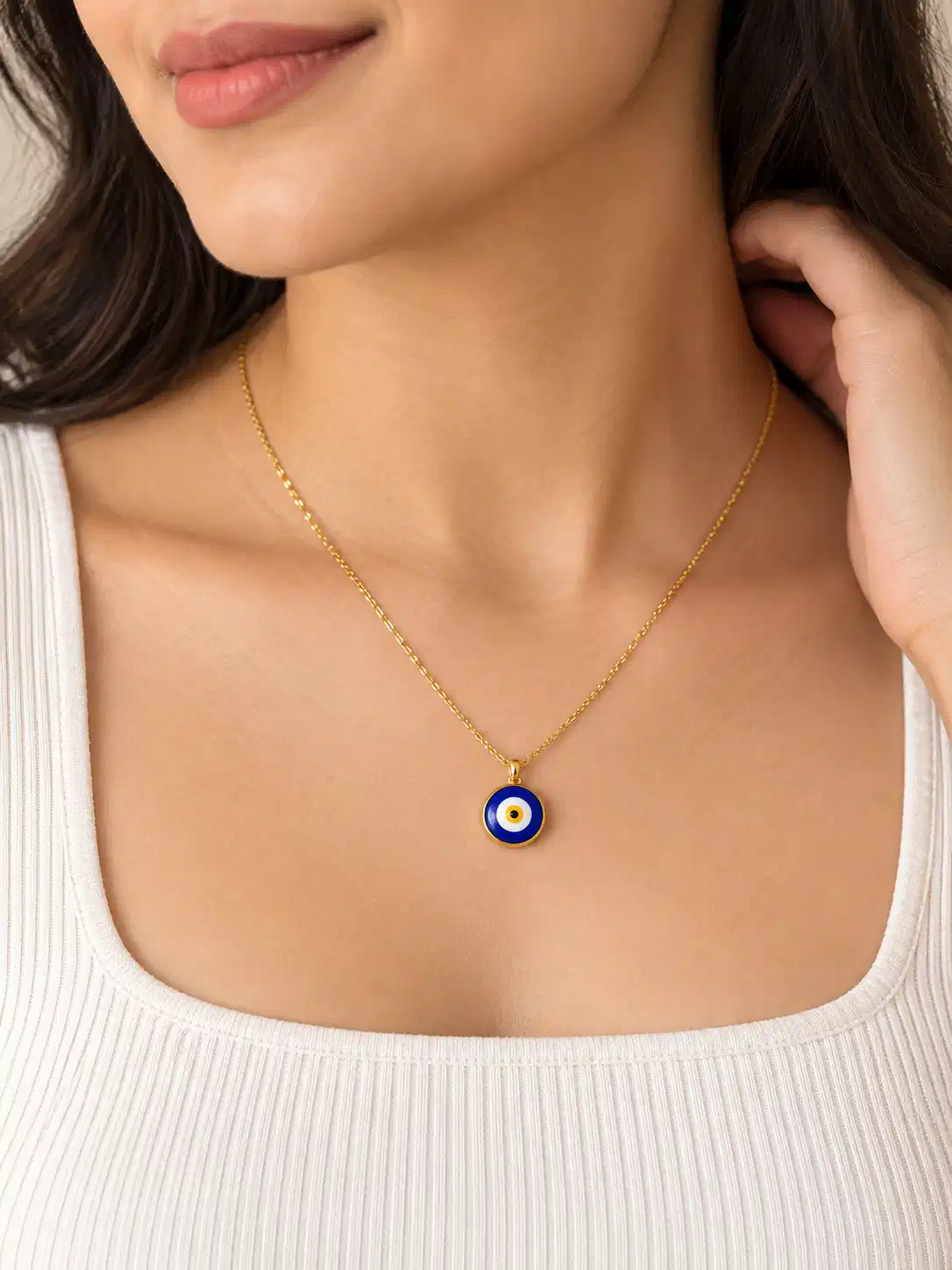 Woman wearing a minimal gold-tone blue evil eye pendant necklace with white square-neck top