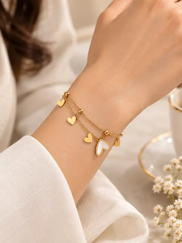 Woman wearing gold layered heart charm bracelet with ivory accents on wrist