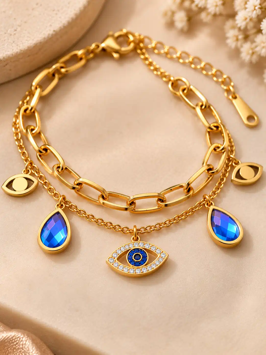 Close-up of crystal evil eye centerpiece and faceted blue teardrop charms on a gold double-layer bracelet.