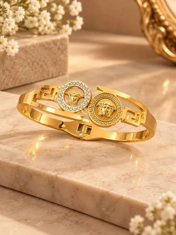 Gold-tone hinged bangle with two circular classical medallions, crystal halo and Greek-key side motifs