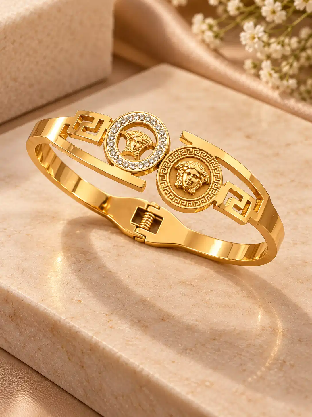 Angled view of gold twin medallion rigid bangle with crystal halo, engraved detailing and spring hinge