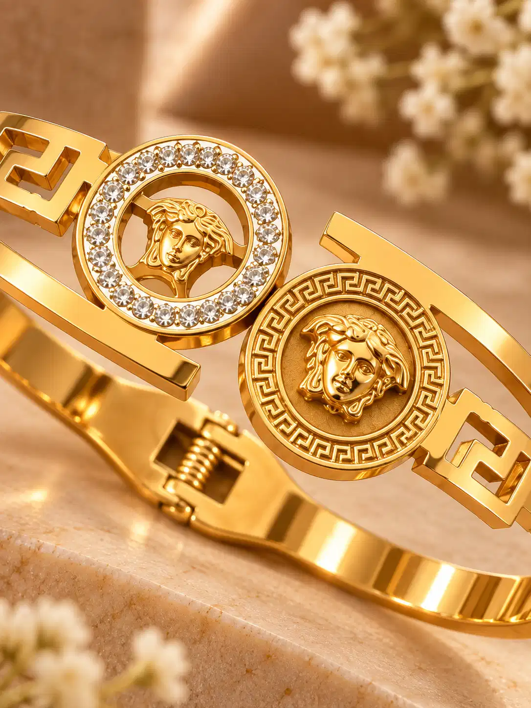 Close-up of twin classical medallions with clear crystal halo and Greek-key engraving on a gold statement bangle